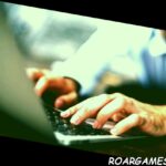 Vista lateral de las manos masculinas escribiendo en el teclado de la computadora portátil