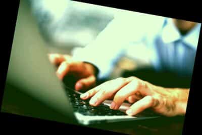 Vista lateral de las manos masculinas escribiendo en el teclado de la computadora portátil